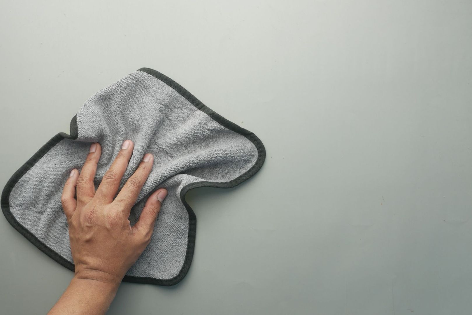 Hand använder en grå mikrofiberduk för skonsam rengöring